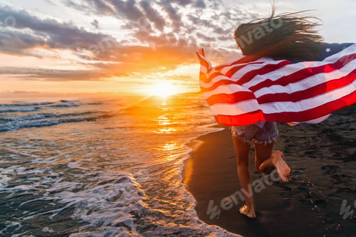 Preview: Happy woman holding american USA flag and running on the beach. Independence Day, travel concept