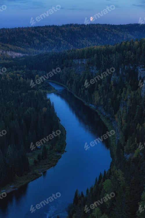 Preview: View of a winding river under the moon at dusk in a forested area