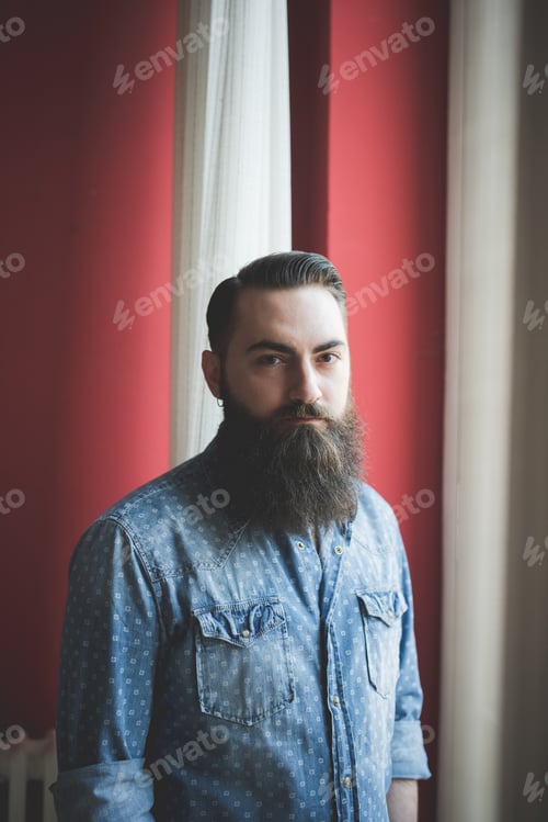 Preview: Young bearded man standing by window