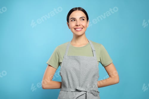 Preview: Young woman in grey apron on light blue background,