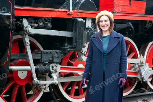 Preview: Young woman in retro styled clothes standing by vintage steam train