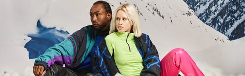 Preview: beautiful multicultural couple in warm bright outfits with mountain backdrop, winter concept, banner