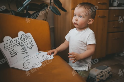 Preview: a child in a white T-shirt stands near an orange sofa and looks at a book