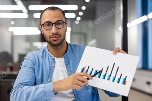Preview: Close-up portrait of a young Hispanic man working in an office, sitting at a desk and showing
