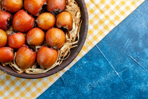 Preview: Half shot of mespilus germanica in a tissue basket in a brown bowl on yellow stripped towel on blue