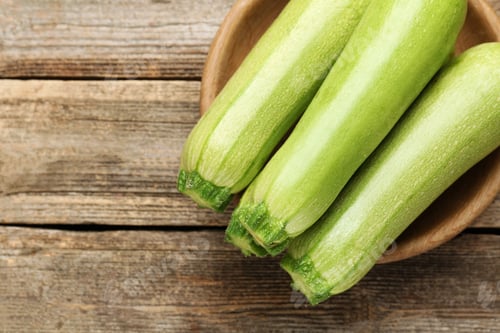 Preview: Fresh ripe zucchinis on wooden table, top view. Space for text