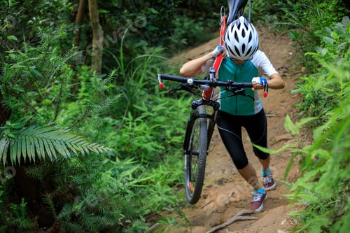 Preview: Woman cyclist carry a mountain bike walking on tropical forest trail