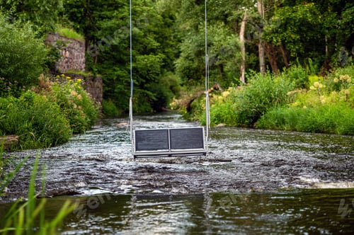 Preview: empty swing hanging on ropes above a fast flowing river, concept of active recreation