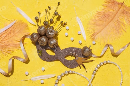 Preview: Carnival mask, beads and feathers on yellow background, top view