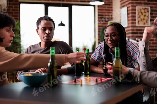 Preview: Multiethnic group of friends sitting at table while playing boardgames with figurines.