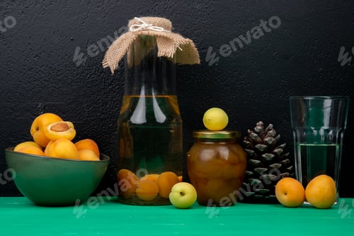 Preview: side view of apricot compote in glass bottle with jam apricots pinecone on green surface