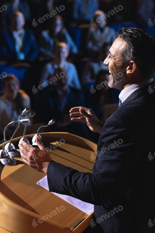 Preview: Side view of Caucasian businessman standing and giving presentation in the auditorium