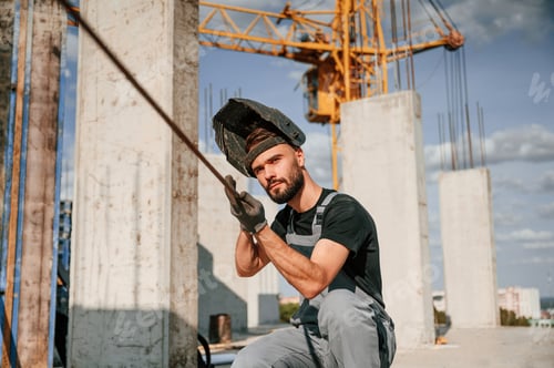Preview: In welding mask. Man in uniform is working on the construction site