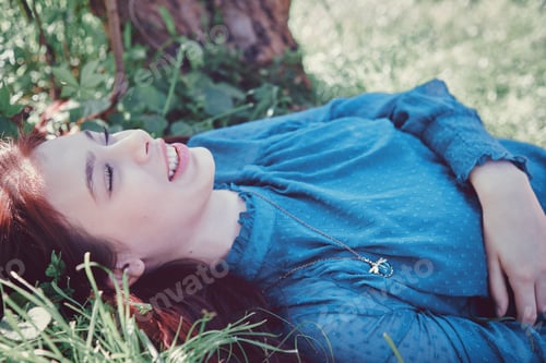 Preview: Young teenage girl lying on grass under trees. Spring leisure concept.