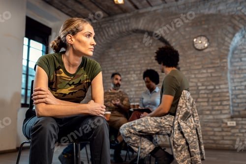 Preview: Female soldier talking with diverse group of veterans during PTSD support group.