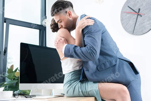 Preview: young passionate business colleagues kissing in foreplay at workplace in office
