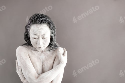 Preview: Art portrait of asian woman covered in clay isolated over grey background. Woman face like cracked p