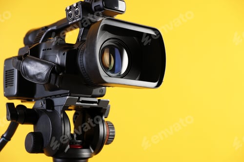 Preview: Modern video camera on yellow background, closeup. Space for text