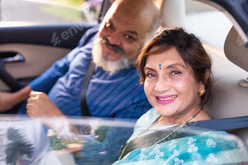 Preview: Senior Indian couple seated in a car, looking outside or at the camera, enjoying a peaceful moment