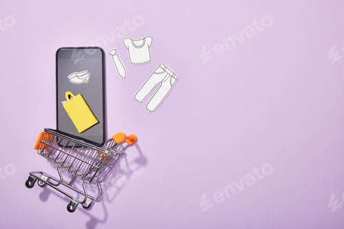 Preview: top view of smartphone with paper cut of clothes and yellow paper bag falling into toy cart on