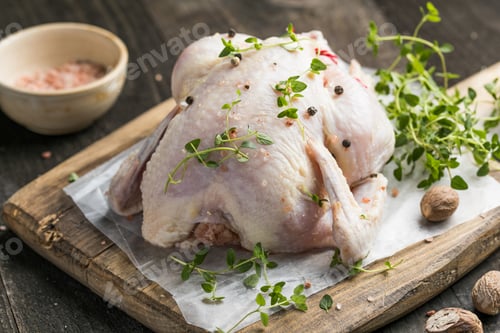 Preview: organic raw whole chicken with thyme peppers and garlic on a rustic table
