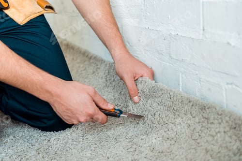 Preview: cropped view of installer holding cutter near carpet