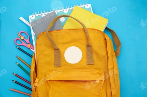 Preview: Backpack on the table with notepads, scissors, colored pencils on a blue background