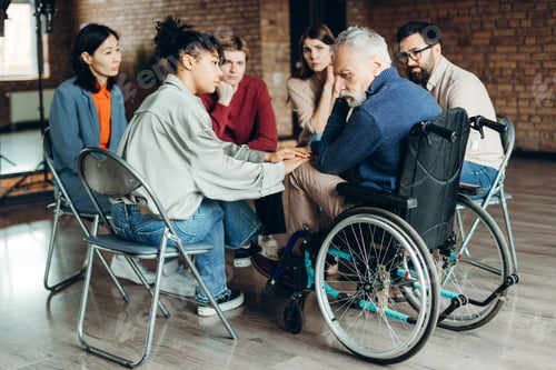 Preview: Psychotherapist comforting senior man in wheelchair during group therapy session