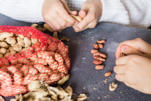 Preview: Peanut kernels, a mesh bag with nuts and husks on the table. Children's hands are peeling nuts