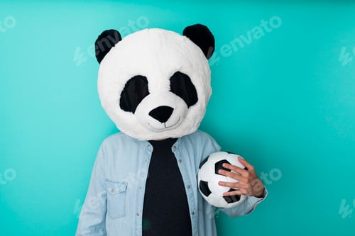 Preview: Man in panda mask holding football ball over blue background - Sports concept