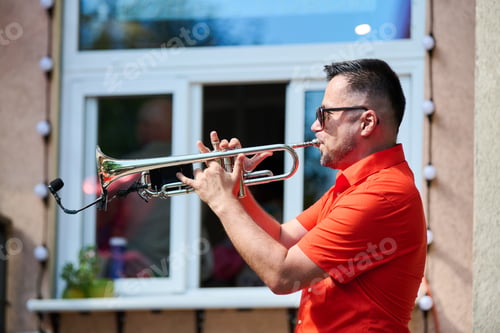 Preview: Adult man playing trumpet outdoors in bright daylight near window