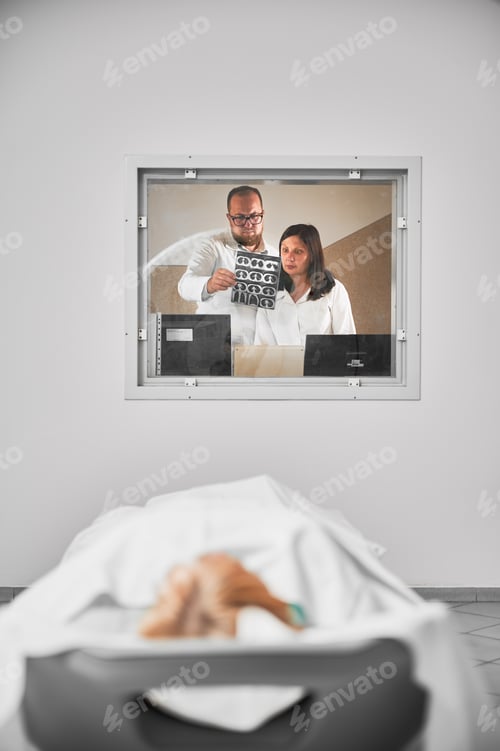Preview: Doctor and nurse looking at MRI results, patient lying.