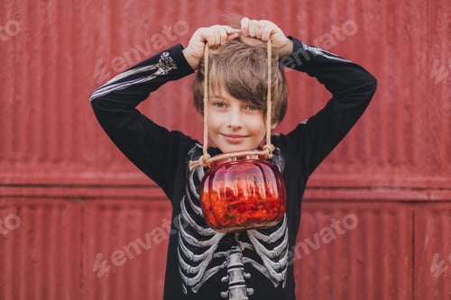 Preview: A boy in a halloween skeleton costume stands on a green background and holds a pumpkin with sweets i