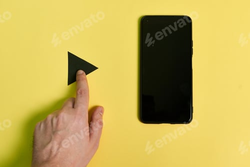 Preview: A man's hand touches a playback button with a phone next to it on a yellow background