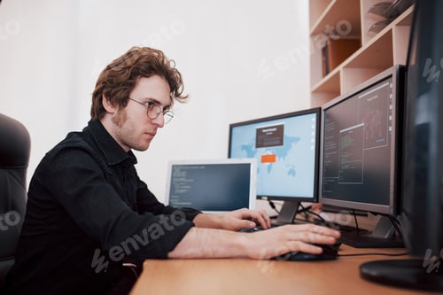 Preview: Male programmer working on desktop computer with many monitors at office in software develop company