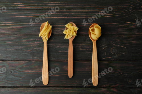 Preview: Spoons with uncooked pasta on wooden background