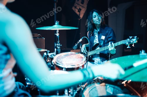 Preview: Female musician playing bass guitar with drummer in recording studio