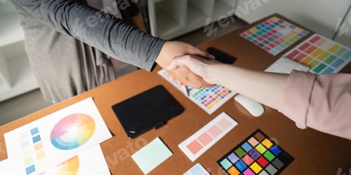 Preview: Close-up of graphic designers shaking hands over a desk with color palettes.