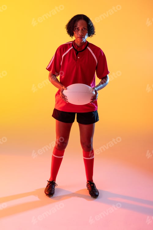 Preview: Portrait of african american female rugby player with rugby ball over neon yellow lighting