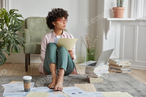 Preview: Photo of thoughtful bare foot female financier compares prices in paper documents, prepares monthly