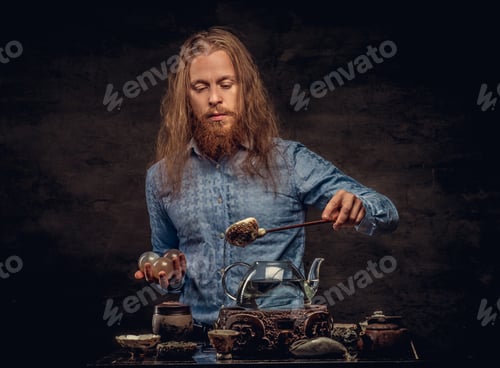 Preview: Bearded redhead male in a blue shirt preparing tea