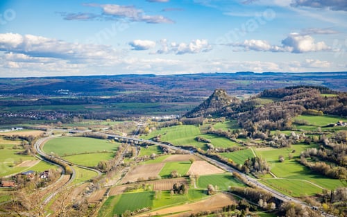 Preview: Hilly area with forests, fields, houses and highways in sunlight against a cloudy sky