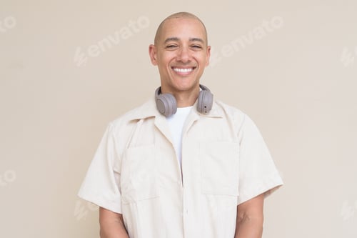 Preview: Bald Latin man in casual shirt with headphones around neck against beige background