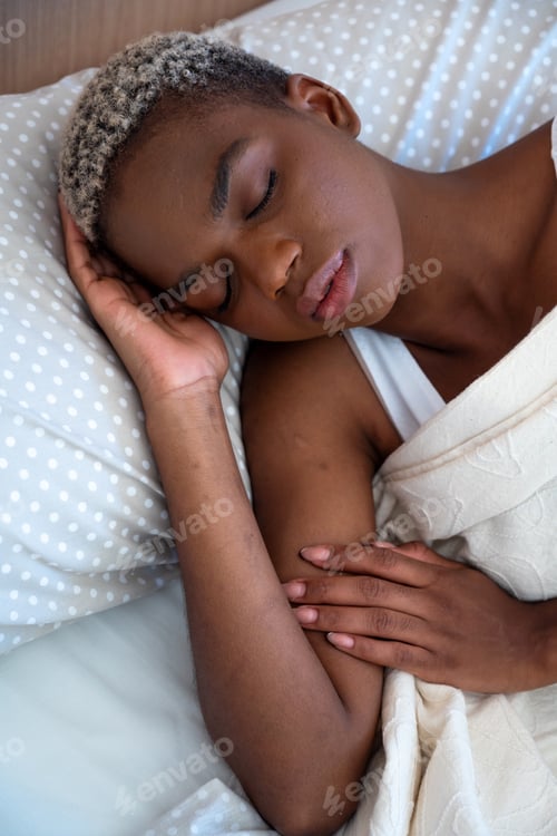 Preview: Calm black woman lying in soft bed under blanket and sleeping in morning