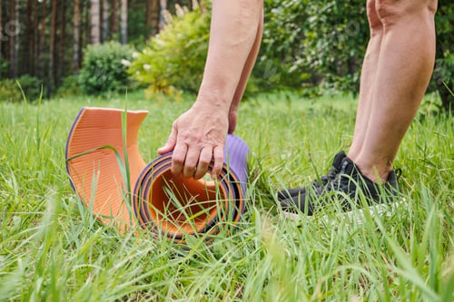 Preview: Mature woman getting ready to exercise and laying out mat at public park close up