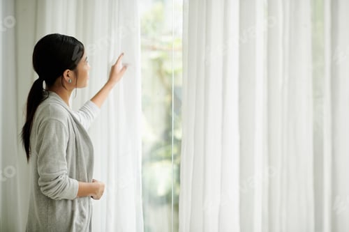 Preview: Woman Looking Out Window at Home During Daytime