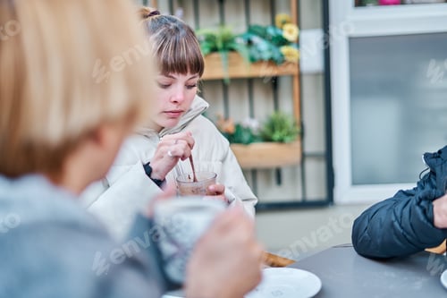 Preview: female friends sitting in a bar terrace wearing a coat having a cup of coffee and cocoa drink