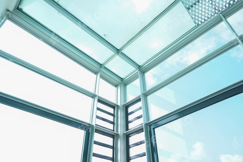 Preview: Low angle shot of the sky visible through the glass walls and ceiling of a modern building