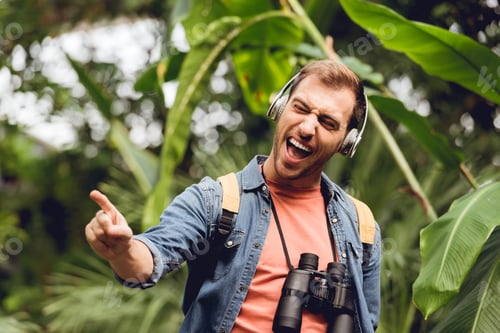 Preview: excited traveler with backpack and binoculars listening music in headphones and singing in tropical