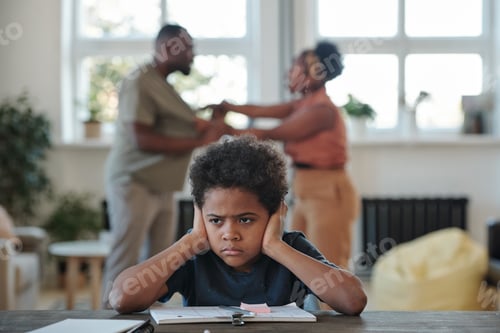 Preview: Angry little boy of African ethnicity covering his ears by hands while trying to do home assignment
